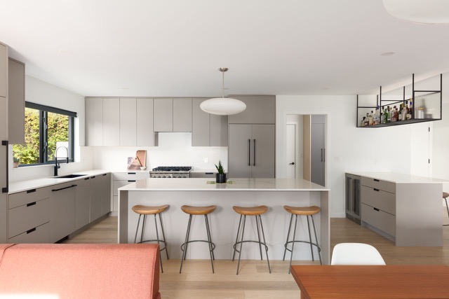 Main floor after — open kitchen with island and barstools, greige cabinetry and light oak floors